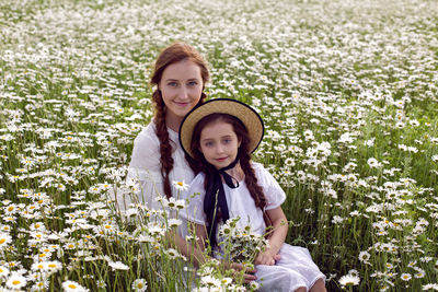 Mother with daughter in a white dress and hat stand in a daisy field in summer