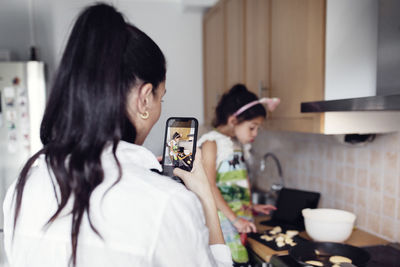 Girl photographing daughter in kitchen