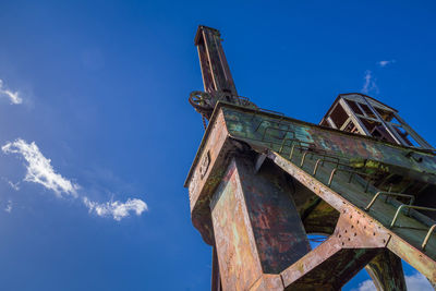 Low angle view of old-fashioned crane against blue sky