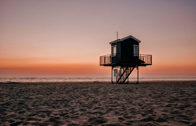 Lifeguard hut on beach against sky during sunset