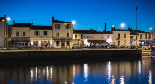 River by illuminated buildings against sky at dusk