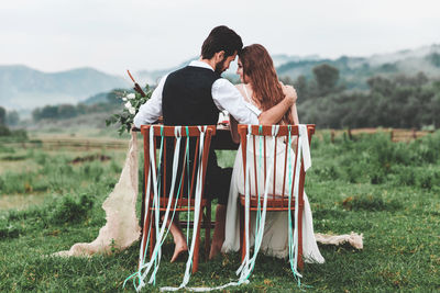 Rear view of wedding couple sitting on chairs at farm