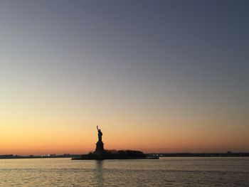 Statue in sea at sunset