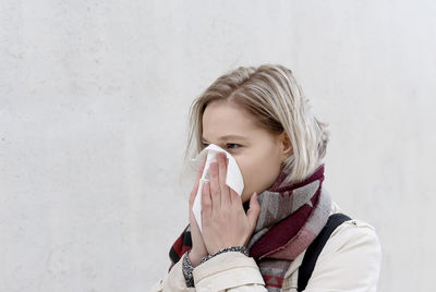 Young woman blowing nose while standing against wall