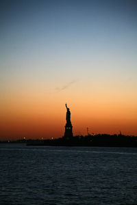 Statue of liberty by sea against sky during sunset