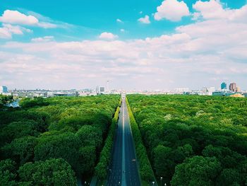 High angle view of street amidst trees towards city against cloudy sky