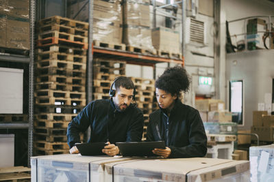 Male and female colleagues discussing while using digital tablet at logistics warehouse