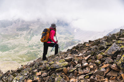 Woman traveler goes to the top of the mountain. a girl with trekking poles and a backpack stopped to