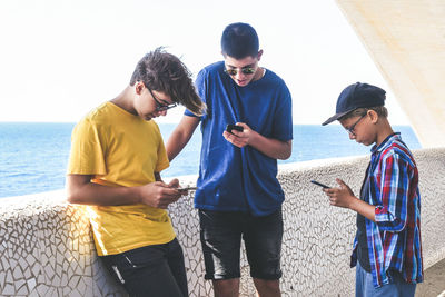 Friends using mobile phone against sea