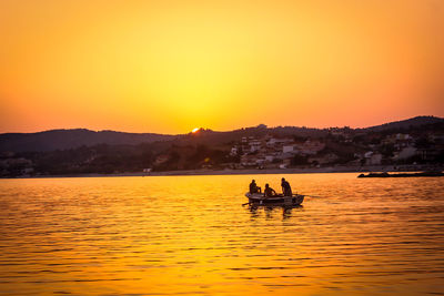 Men riding boat on lake against clear sky during sunset