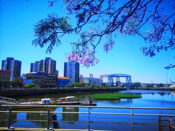 Modern buildings by river against blue sky