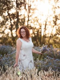 Mature woman holding flower between cereal plants looking away