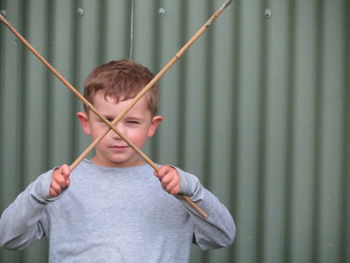 Close-up of boy playing with sticks against corrugated iron