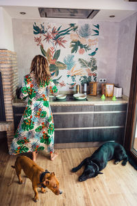 High angle of loyal dog resting on floor near barefoot woman in colorful dress cooking healthy lunch in light kitchen at home