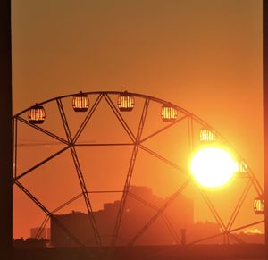 Silhouette ferris wheel against orange sky