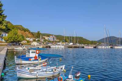 Boats moored at harbor against clear blue sky