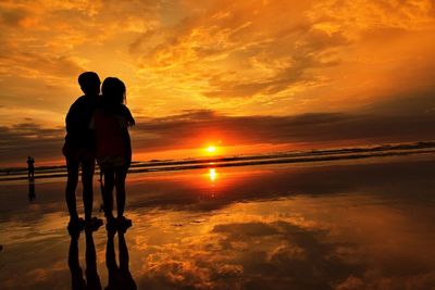 Friends standing at beach against sky during sunset