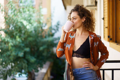 Young woman drinking water while standing outdoors