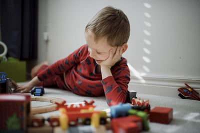 Boy with head in hand playing with model train set while lying on carpet at home