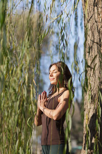 Young woman standing by tree against plants