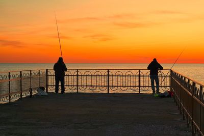 Silhouette men fishing on sea against sky during sunset