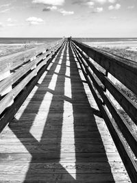 Shadow of wooden railing on beach against sky