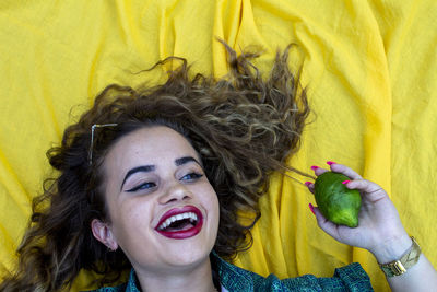 Smiling young woman holding lemon against picnic blanket