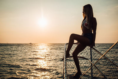 Woman standing at sea shore against sky during sunset