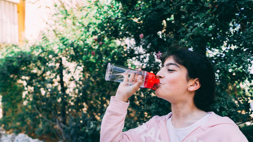 Portrait of young woman drinking drink against trees