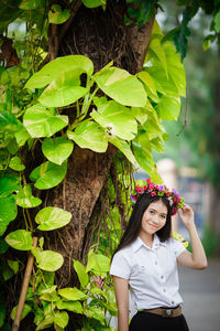 Portrait of woman wearing flowers while standing by tree