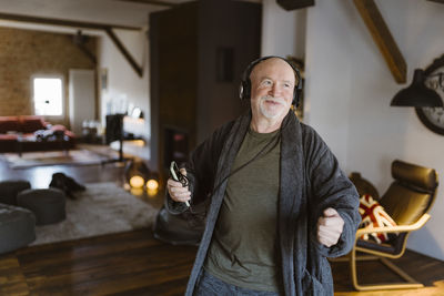 Happy senior man enjoying listening to music over headphones at home