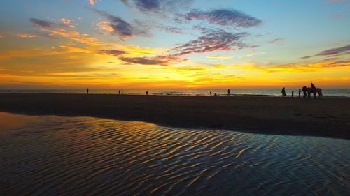 Silhouette people on beach against sky during sunset