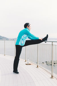 Full length of man standing on railing against sky