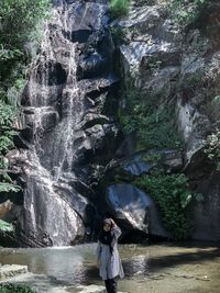 Full length of woman standing on rock against waterfall