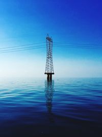 Electricity pylon by sea against blue sky