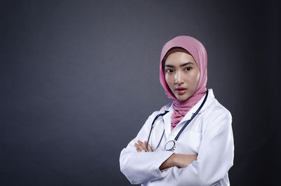 Portrait of doctor standing against gray background