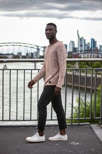 Full length portrait of young man standing against railing in city