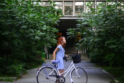 Young woman with bike in front of apartment building and large bush