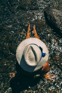 High angle view of woman wearing hat while sitting on rock in sea