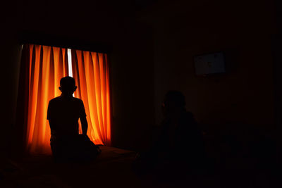 Rear view of silhouette man sitting in illuminated room