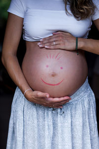 Midsection of pregnant woman making anthropomorphic smiley face on stomach