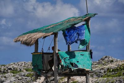 Man sitting in abandoned hut against sky