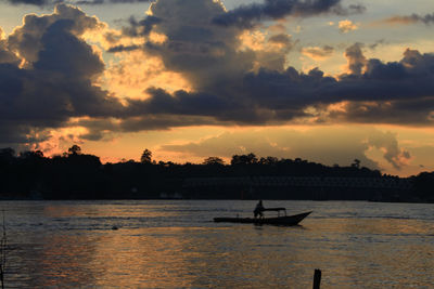 Silhouette person on sea against sky during sunset