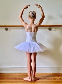 Rear view of ballet dancer with arms raised standing against wall