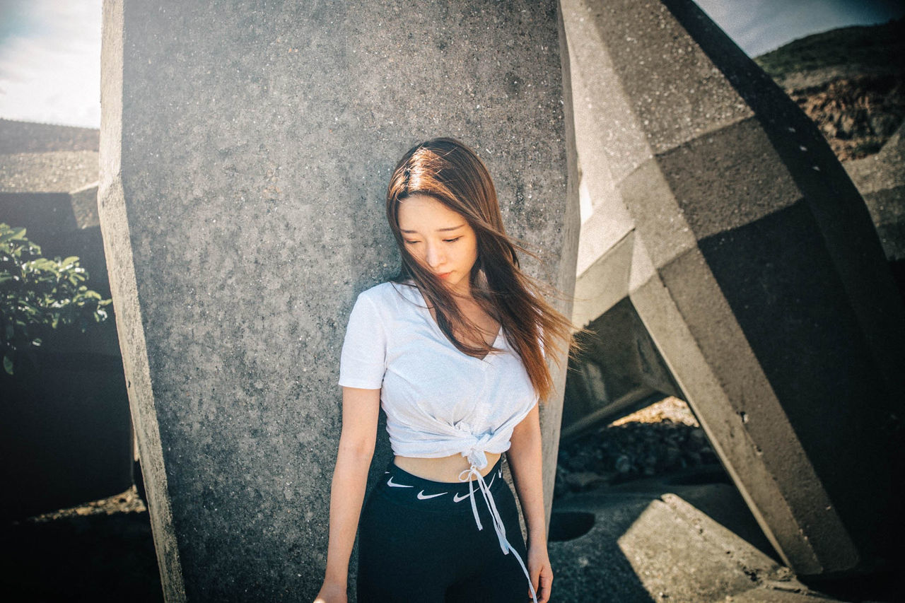 FULL LENGTH OF YOUNG WOMAN STANDING AGAINST WALL