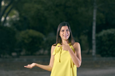 Portrait of smiling woman gesturing while standing against trees on road