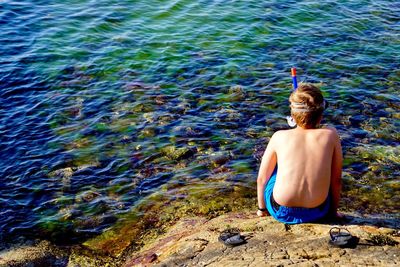 Rear view of shirtless man sitting by lake