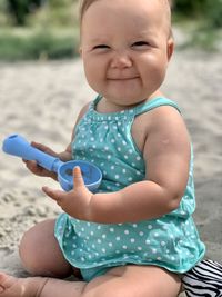 Smiling baby in a tourquoise polka-dot dress playing with sand at the beach in a sunny day 