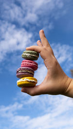 Midsection of person holding macaroons against sky