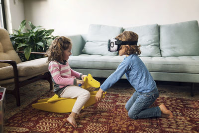 Boy wearing virtual reality simulator playing with sister sitting on rocking horse at home